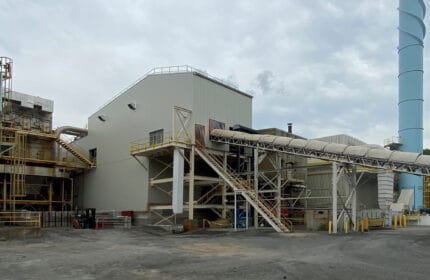 USG Interiors - Manufacturing Facility Exterior View of Conveyor System, Building, Stack